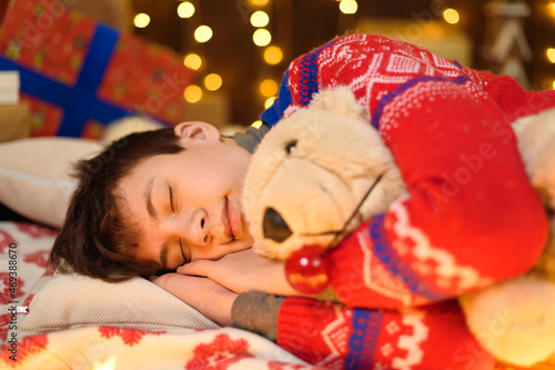 Portrait of teenage boy sleeping in new year or christmas decoration. Holiday lights, gifts and christmas tree decorated with toys.
