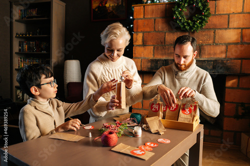 Cheerful young family making Christmas advent calendar together sitting at table on background of fireplace in cozy house on xmas Eve  enjoying togetherness preparing for holidays at home.