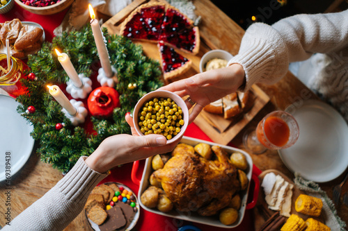 Foto Close-up high-angle view of unrecognizable young woman and man passing delicious food sitting at festive Christmas table during holiday family friendly party, selective focus