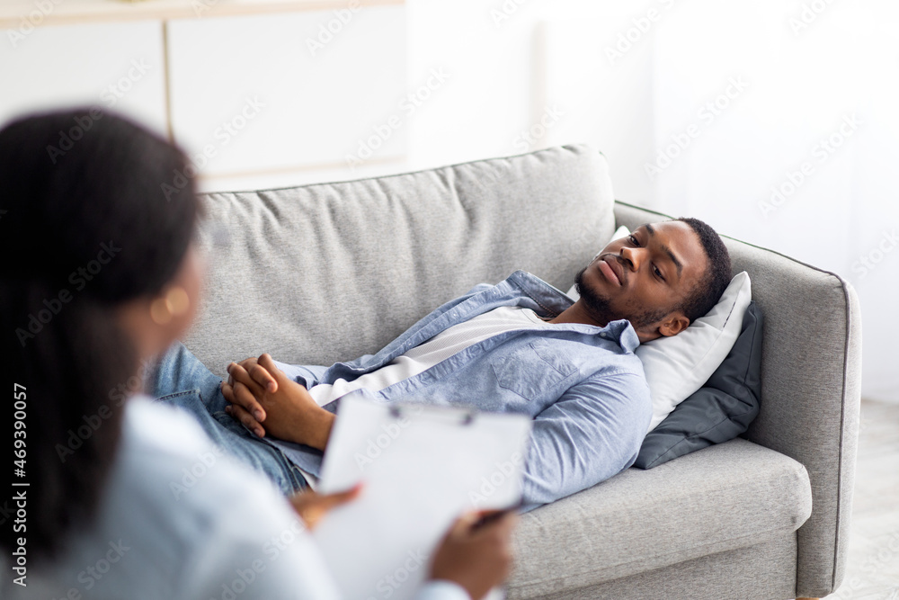 African American male patient lying on couch at psychologist's office, having session with counselor