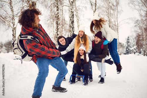 Group of happy men and women spending time in winter woods having fun on sleigh