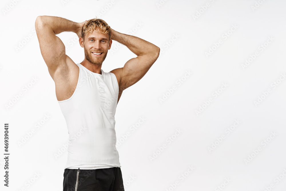 Smiling sportsman in activewear, holding hands behind head and flexing biceps, showing strong arms, workout, standing over white background Smiling sportsman in activewear, holding hands behind head and flexing biceps, showing strong arms, workout, standing over white background