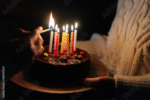Sticker Close-up of unrecognizable man burning candles, woman holding in hands birthday cake with six burning candles in dark room