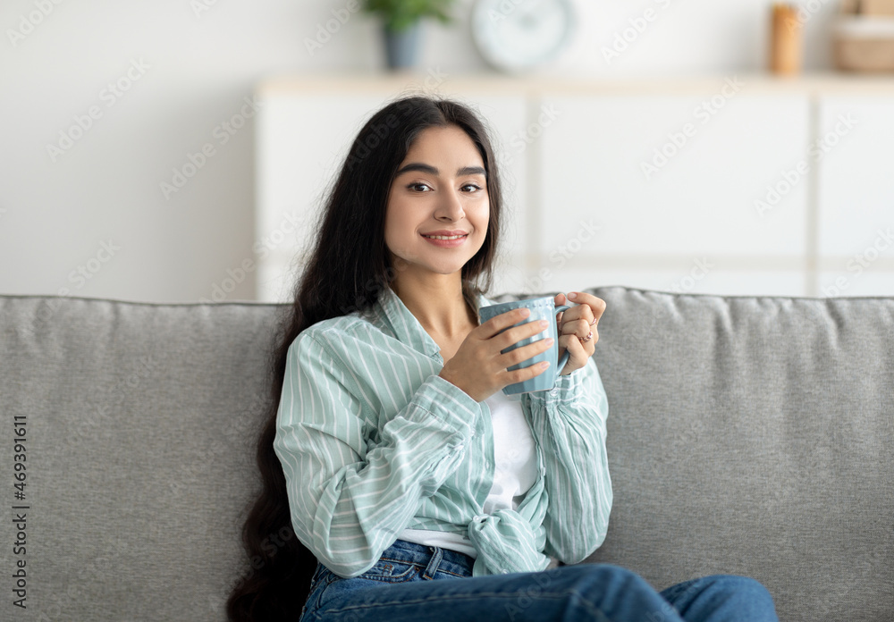 Portrait of beautiful peaceful Indian woman relaxing on couch with cup of fresh coffee at home Portrait of beautiful peaceful Indian woman relaxing on couch with cup of fresh coffee at home