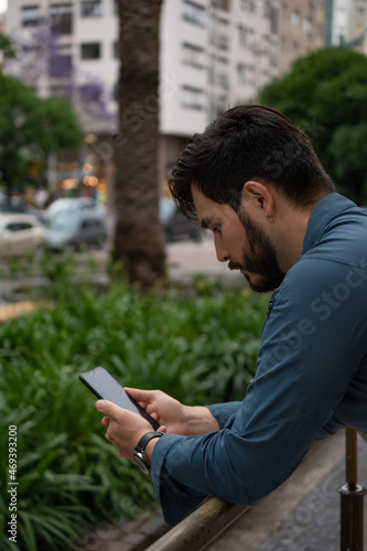 Businessman leaning on a railing  looking at his cell phone. In a downtown square