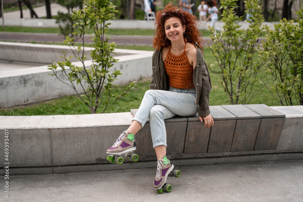 happy and curly roller skater smiling at camera on bench in skate park. happy and curly roller skater smiling at camera on bench in skate park.