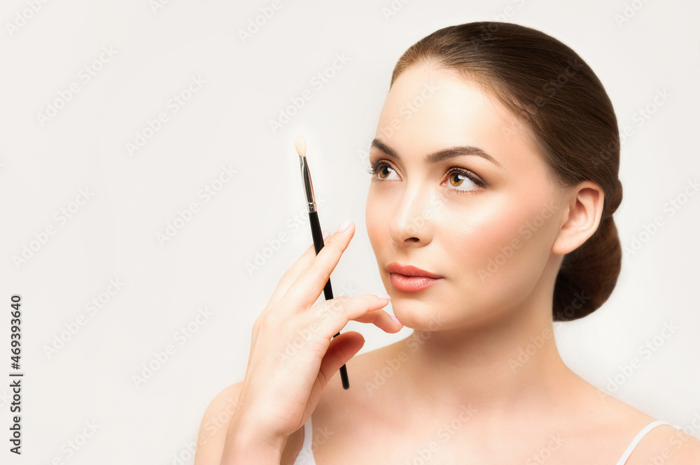 Model doing makeup. Caucasian girl thinks about make-up with brush in her hand Model doing makeup. Caucasian girl thinks about make-up with brush in her hand