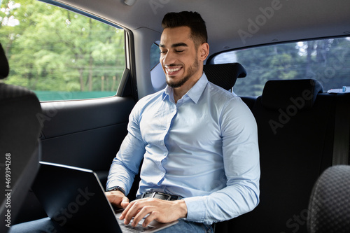 Cheerful middle eastern businessman working at car, using laptop © Prostock-studio