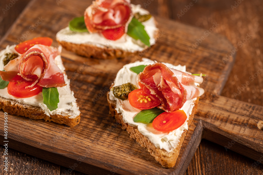 Open sandwich toast with cheese cream, prosciutto ham and greens on wooden board and wooden background