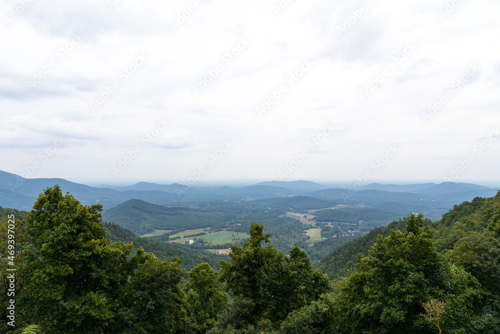 Scenic overlook of the Blue Ridge Mountains on a hazy, overcast day, deep green tree line in the foreground, horizontal aspect