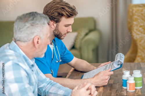 Serious geriatrician prescribing multivitamins to a gray-haired man photo