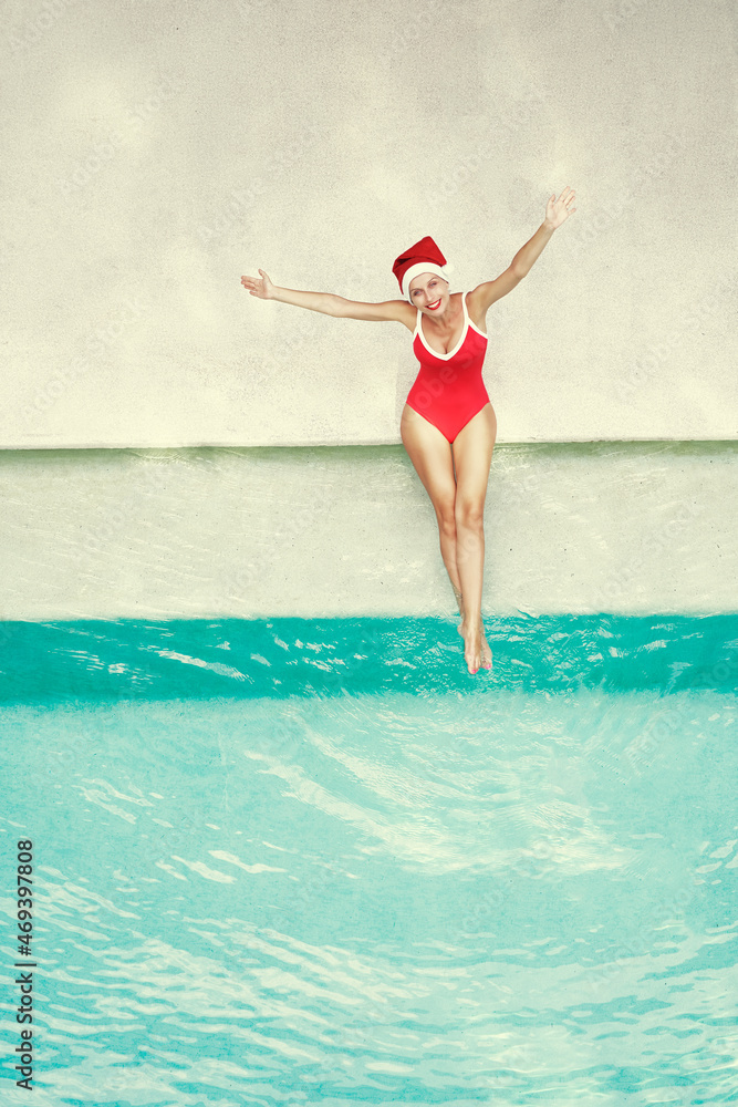 Enjoying christmas holidays and vacation. Top view of excited young woman in red swimsuit  and  santa claus hat rising hands up near swimming pool.