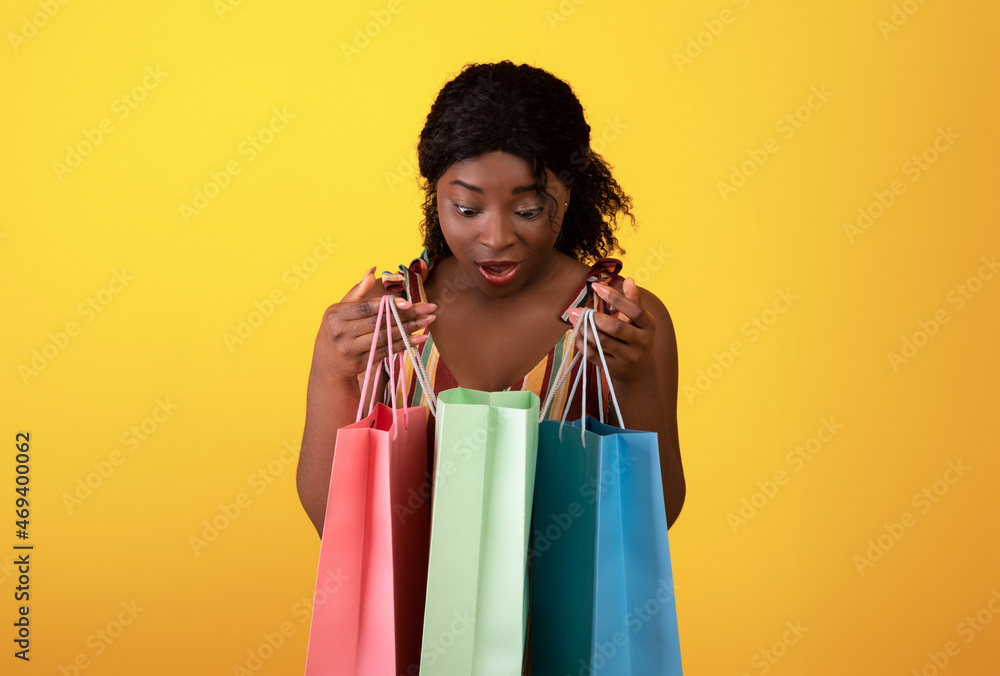 Shocked black woman looking inside shopping bags, feeling surprised on orange studio background Shocked black woman looking inside shopping bags, feeling surprised on orange studio background