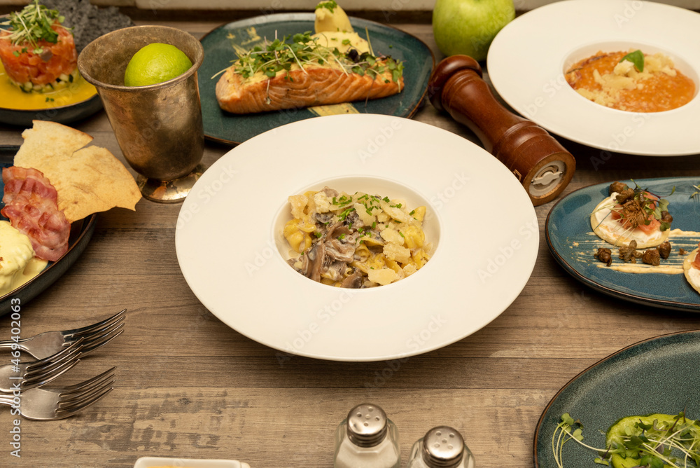 Set of international food dishes on dark wooden table. Blisines, pasta with parmesan, grilled Norwegian salmon, tuna tartare, eggs benedict Set of international food dishes on dark wooden table. Blisines, pasta with parmesan, grilled Norwegian salmon, tuna tartare, eggs benedict