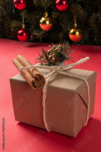details of one gift box wrapped and decorated with a bow of cord and cinnamon stick, studio with pink background and a Christmas arbold with spheres, surprise object photo