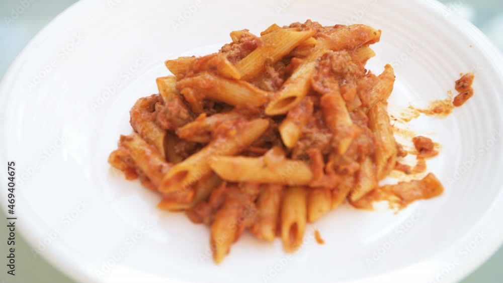 Rack focus macro closeup of fresh red tomato sauce marinara and ground lamb or beef hamburger meat bolognaise with penne pasta noodles on white plate background Rack focus macro closeup of fresh red tomato sauce marinara and ground lamb or beef hamburger meat bolognaise with penne pasta noodles on white plate background