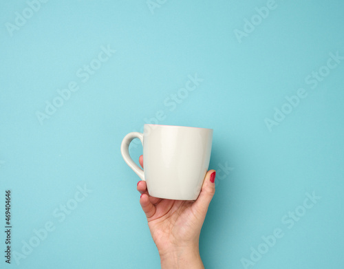 female hand holds a ceramic mug on a blue background  break time and drink coffee