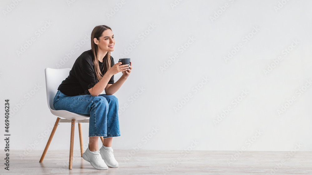 Leinwandbild Motiv - Prostock-studio : Coffee break. Dreamy young woman sitting on chair, enjoying cup of hot beverage against white wall, copy space