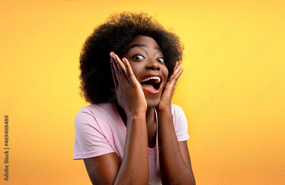 Wow offer. Overjoyed african american lady looking at camera in excitement and touching face over yellow background Wow offer. Overjoyed african american lady looking at camera in excitement and touching face over yellow background