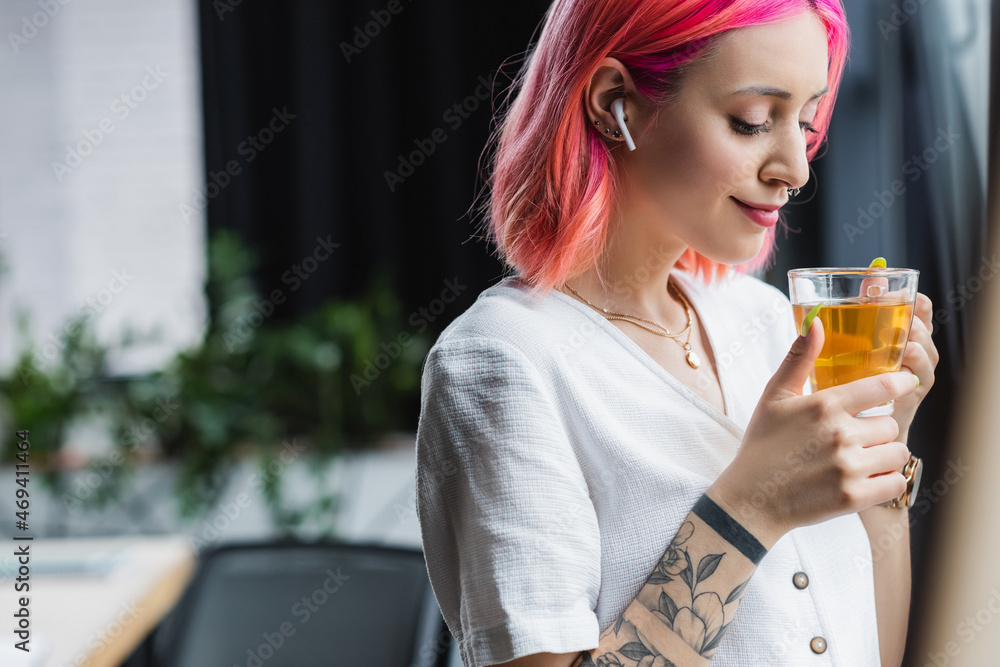 pleased businesswoman with pink hair and earphone holding cup of tea in office. pleased businesswoman with pink hair and earphone holding cup of tea in office.