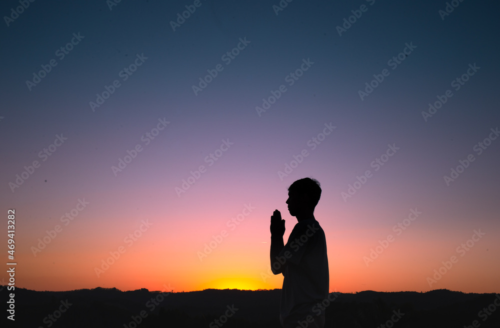 Silhouette of a man praying and thanking God with the sunset sky in the background. Concept of faith and spirituality.