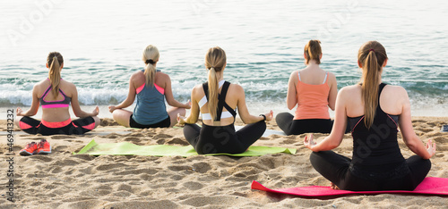 Back view of young women practicing various yoga positions on beach