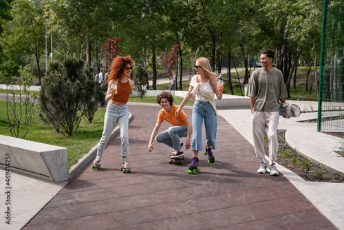 smiling african american man walking near happy friends skating in park.