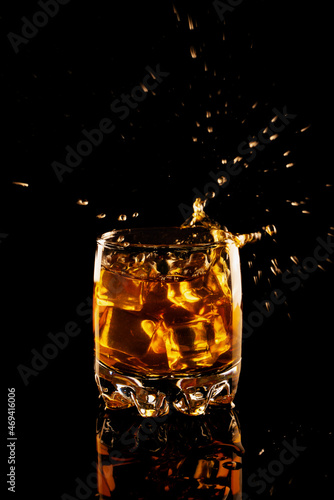 glass of whiskey with ice and splash on a black background