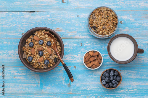 Muesli in a clay bowl, milk, nuts and berries on a blue wooden table. Flat lay.