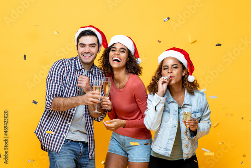 Party time portrait of happy diverse friend group with champagne celebrating Christmas on yellow studio background with confetti