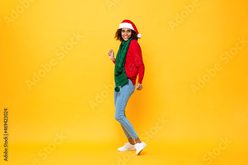 Excited happy woman in Christmas attire dancing in isolated yellow studio background