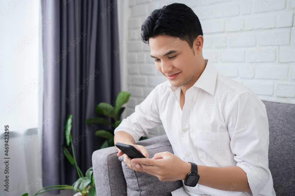 Handsome Asian Man Using Smartphone While Relaxing Leaning On Couch At Home Handsome Asian Man Using Smartphone While Relaxing Leaning On Couch At Home