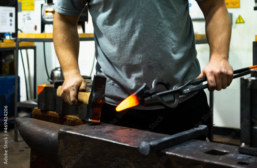 A blacksmith holds a glowing hot piece of metal shaped into a V and prepares to hit it with a hammer A blacksmith holds a glowing hot piece of metal shaped into a V and prepares to hit it with a hammer