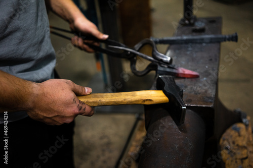 A blacksmith holds a hammer and a hot piece of metal with a pair of tongs on an anvil