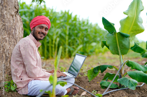 Young indian farmer using laptop at agriculture field.
