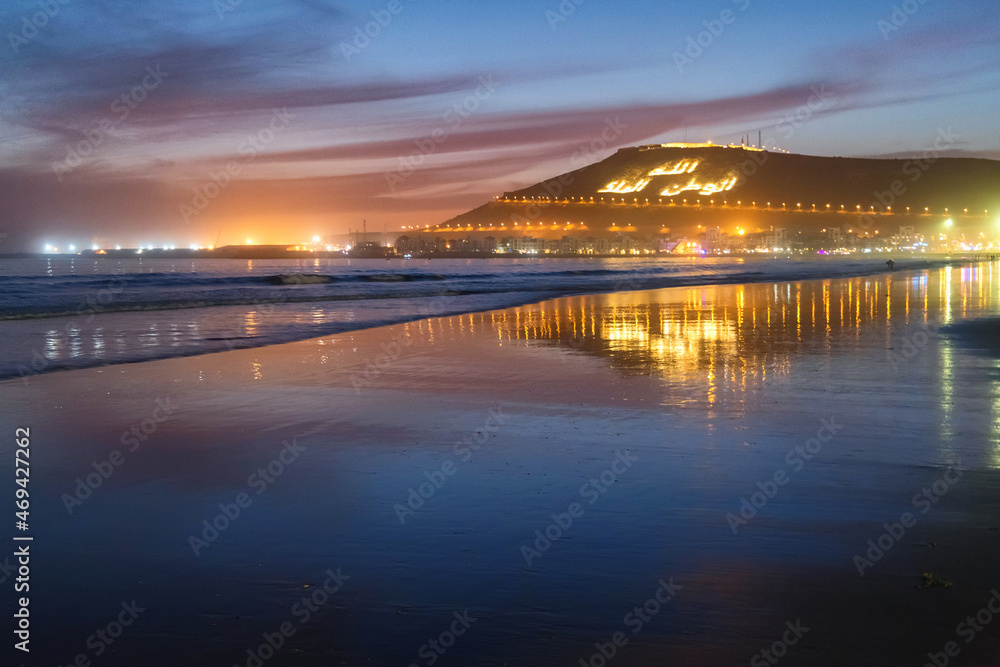Fototapeta premium Beautiful evening view of the Atlantic ocean coast in Agadir, Morocco. With Kasbah mountain on the background with inscription in Arabian: Allah, The King, One's native land.