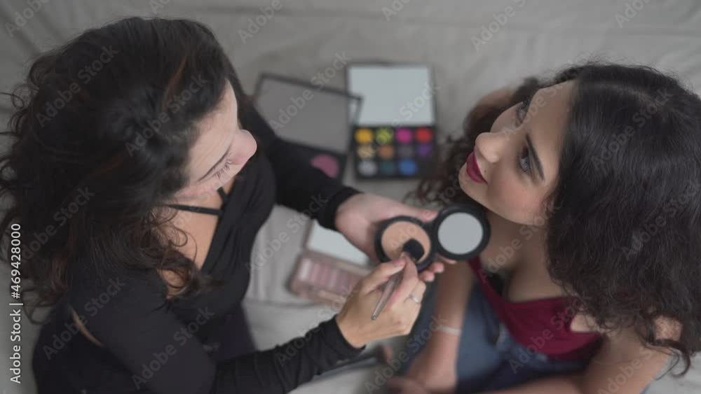High-Angle View Of Two Colombian Women Sitting On Bed Having A Makeup Session, Preparing For A Halloween Party In Valencia, Spain. - High-Angle Shot High-Angle View Of Two Colombian Women Sitting On Bed Having A Makeup Session, Preparing For A Halloween Party In Valencia, Spain. - High-Angle Shot