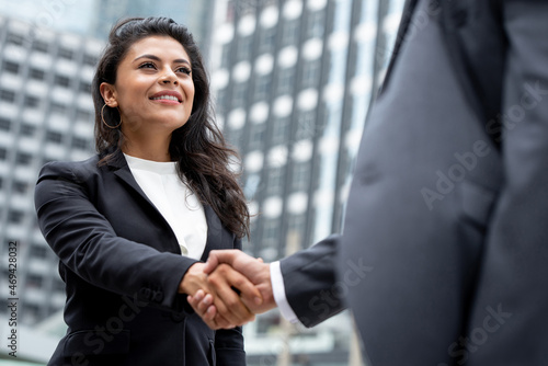 Young smiling Hispanic businesswoman making handshake with partner in the city for greeting, dealing, merger and acquisition concepts photo