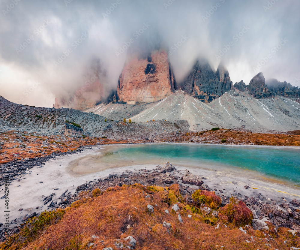 Naklejka premium Tre Cime Di Lavaredo peaks in the morning mist. Picturesque autumn view of frozen Rienzquelle lake. Gloomy outdoor scene of Dolomite Alps, Italy, Europe. Beauty of nature concept background..
