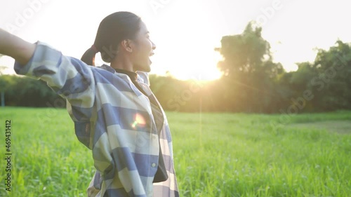 Young asian girl feeling happy and fresh standing on the green grass field enjoy warm morning light, good way to start a day, golden hour with sun light on the background, nature happiness sustainable