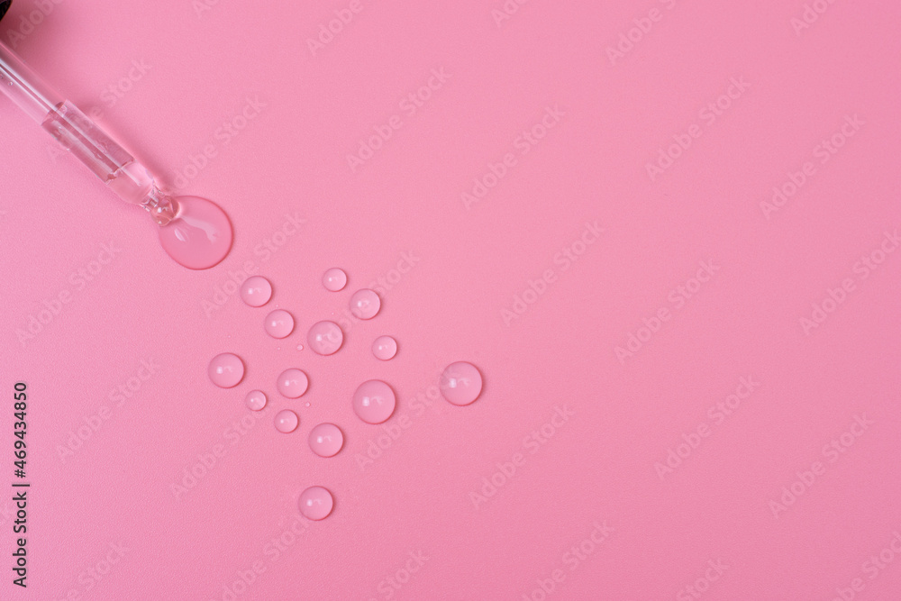 Drops of transparent liquid are squeezed out of a pipette on a pink background