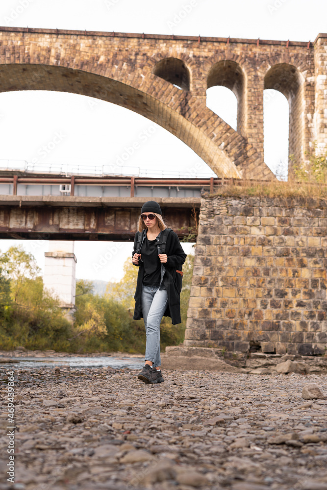 Arched old stone bridge, girl tourist walking by the river, hiking trekking, railway bridge background, tourism and travel.