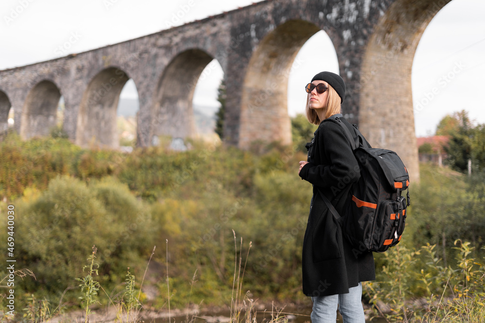 Girl traveler near the old arch bridge traveling through Europe, stone bridge on the background, tourist on a trip in nature.