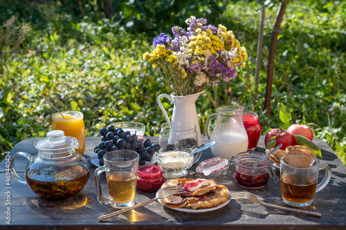 Tea, pancakes, milk and jam on the breakfast table in the autumn garden, close up