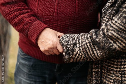 Senior man in love holding and caressing tender hands of his beautiful woman, husband warming cold wrinkled arms of wife during walk along park, couple confessing in love and fidelity, close-up