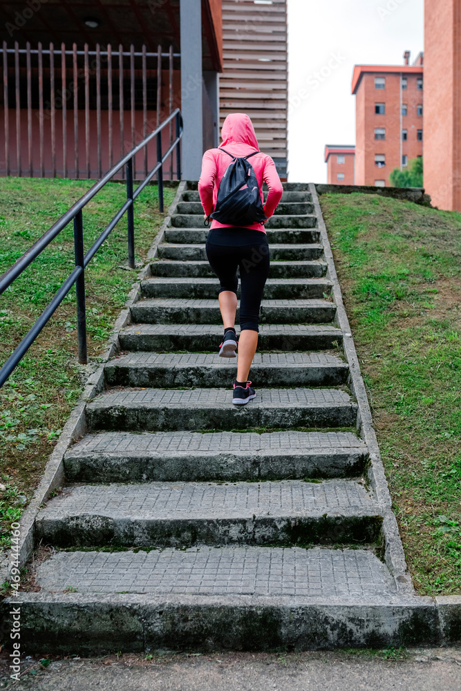 Young female athlete with backpack going up stairs outdoors