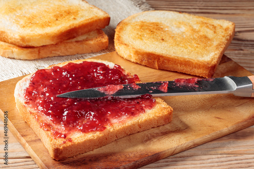 Toast with red jam on wooden board. Selective focus.