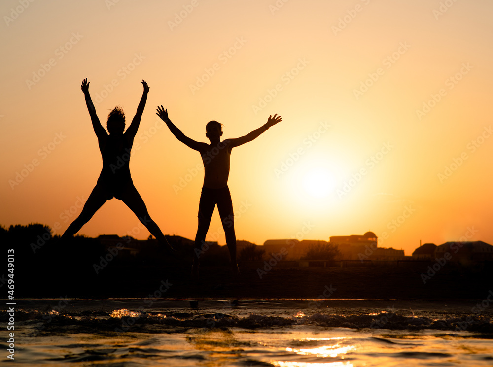 Fototapeta premium Joyful kids are having fun and jump at sunset beach in sunlight. Empty space for text