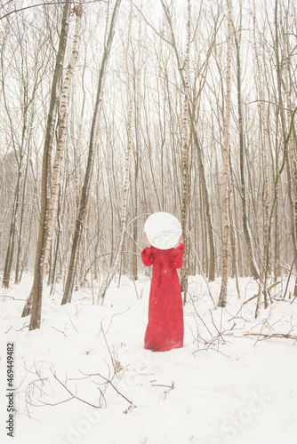 Abstract art portrait of woman in red dress standing in snow in winter forest landscape holding mirror