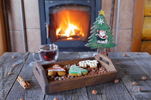 A gingerbread cookies are on a wooden tray in front of fireplace with burning firewood. 